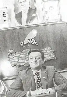 Black and white photo of a middle-aged Turkish man sitting at a desk. He wears a suit and tie.