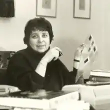 A white woman with short dark hair, wearing a dark tutleneck, seated at a desk