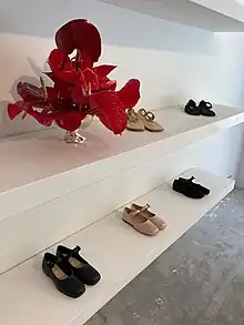 Two white shelves of shoes, with a vase of red flowers