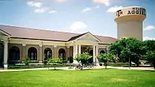 A neoclassical building with columns in front of a water tower sporting the greeting, "Welcome to Aggieland"