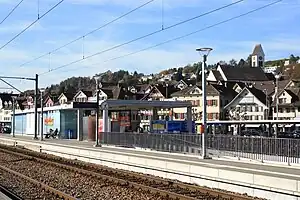 Low platform with boxy structure and houses on a hillside beyond