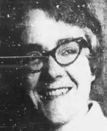 A smiling white woman wearing dark-framed glasses