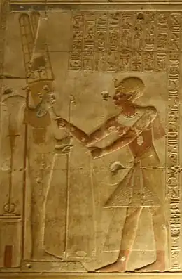 Relief showing an ornately dressed Egyptian man reaching toward a male figure on a pedestal