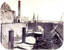 A photograph with two steamships resting in a dewatered drydock with a building housing the engine for operating the lock's gates in the background