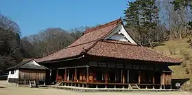 Wooden building with a hip-and-gable style roof and an open veranda surrounding the building.