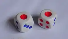 Two cubic dice marked with the Chinese convention, using a single large red pip (for the 1), four smaller red pips (for the 4), and blue pips for the remaining sides. These are displaying 1 and 1 as the face values; the die on the left is also showing the 2- and 3-pip sides, while the die on the right is also showing the 4- and 2-pip sides.