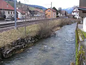 Two-story building with gabled roof and side platform next to single track and flowing river