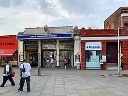 Station entrance with portico and ornamental ironwork signage above stating "Metropolitan and District Railways", "South Kensington station".