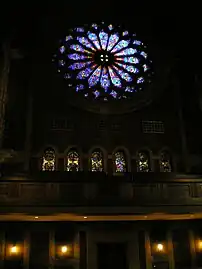 Stained glass rose window over balcony overlooking the pews.