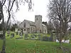 Stone building with square tower. In the foreground are gravestones and trees.