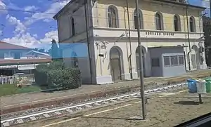 Two-story building with gabled roof next to railway tracks, viewed from a moving train