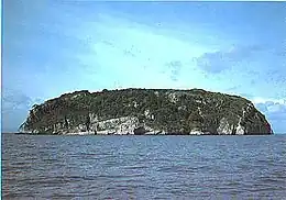 A rocky island with steep sides rises sharply out of the water.