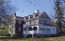 A large stone house with many dormers, windows, and a white porch, surrounded by trees