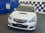 Subaru Legacy tS, a high-performance variant of the standard Subaru Legacy sedan. This photo shows the front of the car, which is white; there is a "tS" badge on the front grille which stands for "tuned by STI".