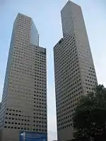 Ground-level view of two identical 45-storey towers with rectangular cross sections; a diagonal cut-out is present on each tower near the 30th floor