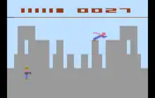 Pixel graphic image that represents a grey city skyline. A blue and red stick figure flies over the city.