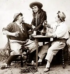 three men in early 19th-century costume, one plump and jolly, one young and dashing and one pouring humself a glass of wine