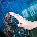 Photo of flowing water adhering to a hand. Surface tension creates the sheet of water between the flow and the hand.