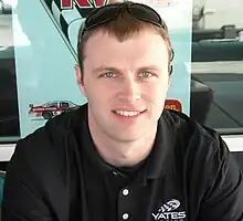 Photograph of a man in his early thirties with a head full of hair, and looking towards the camera.