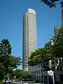 Ground-level view of a 50-storey cylindrical tower with black windows and a small cut-out near the roofline