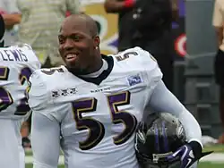 A dark-skinned man holding a football helmet