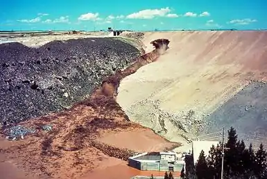 Large amounts of mud are now spilling down the face of the dam, unchecked by the efforts of the bulldozer operators. The outlet works at the foot of the dam are flooding with muddy water.