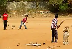 Three Hyderabadi boys playing with cricket bats and a ball