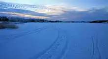 The lake covered with snow, in which tracks of tires and skis are visible