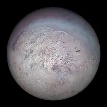 A large spherical object is half-illuminated from the bottom-left. The south pole faces to the light source. Around it in the bottom-left part of the body there is a large white area with a few dozens dark streaks elongated in the pole to equator direction. This polar cap has a slight red tinge. The equatorial region is darker with a tint of cyan. Its surface is rough with a number of craters and intersecting lineaments.