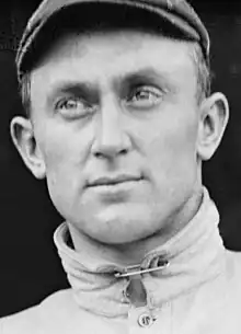 Black and white portrait of a man wearing a high collar, held closed with a safety pin.