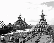 Two large battleships sailing toward the viewer. Personnel can be seen on the decks of both ships.