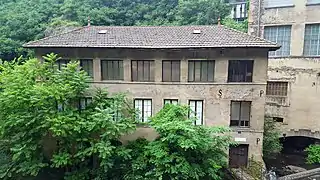 Front view of the 3-storey Entraygues plant with its 7 large square or rectangular windows per floor and dark tiled roof, trees in the foreground.