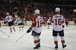 Canadian male in white uniform and white helmet standing next to European male also in white uniform and helmet