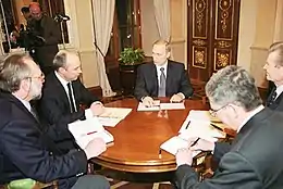 five men in suits gathered around a table