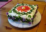 Smörgåstårta with cream-cheese icing and chives, boiled egg yolk, wood-sorrel leaves, tomatoes and flowers for decoration