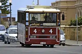 Maroon antique-style bus with cream roof in front of traffic on a road