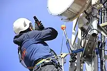 A worker using a personal RF safety monitors on a mast, near antennas.