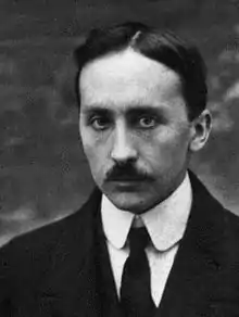 Black-and-white portrait of a man with dark hair and moustache wearing a dark jacket, light shirt, and dark tie