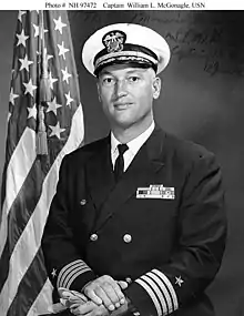 Top half of man in circa 1970 U.S. Navy officer uniform, before an American flag.