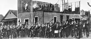 Photograph of armed people by a ruined building