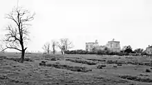 A grassy field with sheep and a stone building in the background.