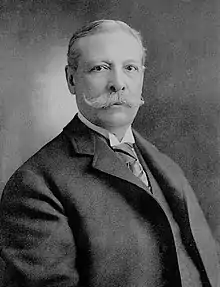 Portrait of Charles Yerkes wearing a frock coat, wing collar shirt and with a large handlebar moustache.