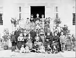 Family photograph of Pontians at a house. Some old women wear traditional clothes. A young boy holds a rifle.