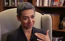 Salbi smiling and speaking while sitting in a chair, filled books shelves in the background