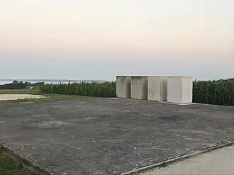 Four concrete blocks stand on a concrete pad, surrounded by undulating grassy land and cornfields.